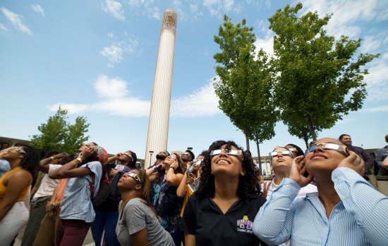 A crowd of people wearing eclipse glasses looks up at the sky under the UAlbany Carillon ahead of the 2017 solar eclipse.