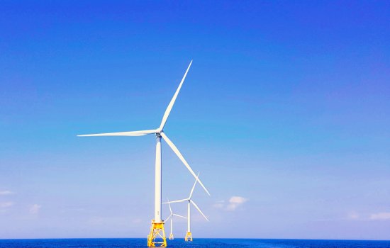 Three white wind turbines emerge from blue water against a blue sky.