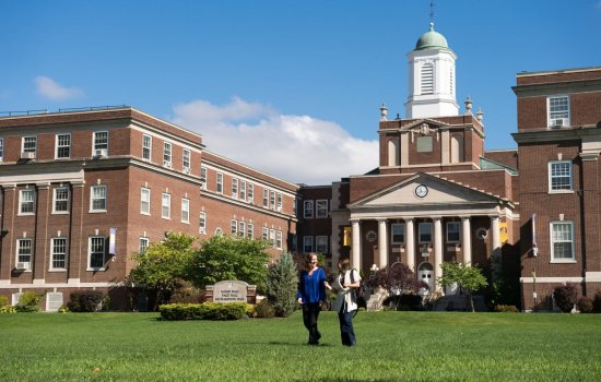 Two students walk on the grass in front of UAlbany's Downtown Campus on a sunny day.