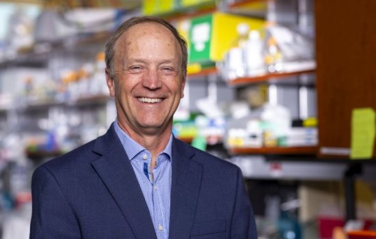 A smiling man in a blue blazer stands in a laboratory.