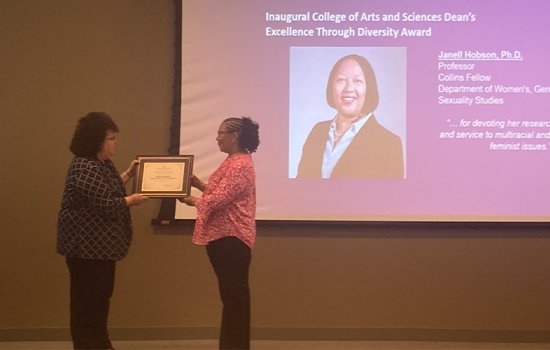 Janell Hobson stands on stage and accepts the inaugural College of Arts and Sciences Excellence Through Diversity Award from Dean Jeanette Altarriba