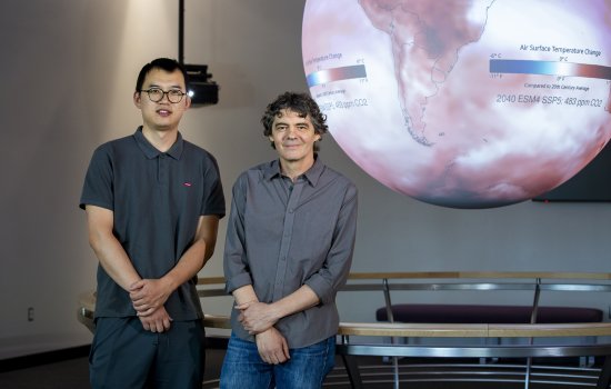 Postdoctoral research associate Zhiqiang Lyu and professor Mathias Vuille of the Department of Atmospheric and Environmental Sciences stand in front of a red and white air surface temperature change map inside the science-on-a-sphere room at ETEC.