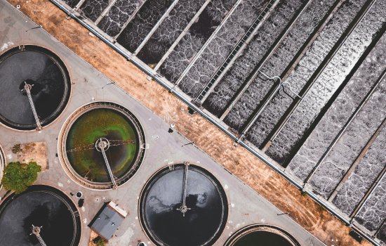 Aerial image of a wastewater treatment facility. The top right half of the image shows water being treated in a rectangular holding pool. On the bottom left, water is held in circular tanks.