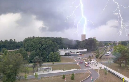 A photo taken from an elevated position showing two flashes of lightning, one of which is striking a rectangular tower in the distance.