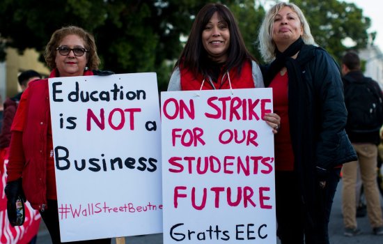 Three women, two of them holding signs that includ the words "Education is NOT a Business" and "On strike for our students' future"