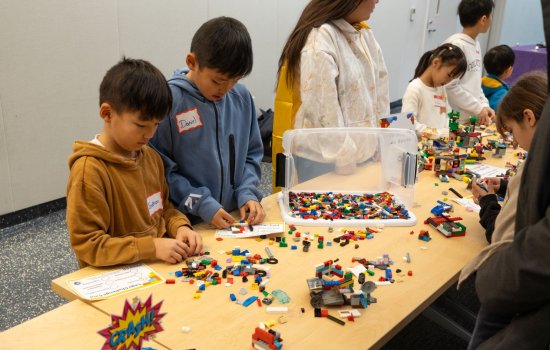 Children work on projects at a table scattered with Lego pieces.