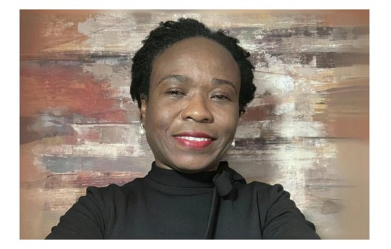 Portrait of a woman with short black hair, red lipstick and pearl earrings. She is smiling and wearing a black top. The background is a faded wood backdrop.
