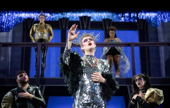 Student actors in hair, makeup and costume sing on stage.