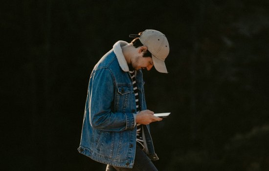 A young man walks outside in nature with his head down staring at an iPhone