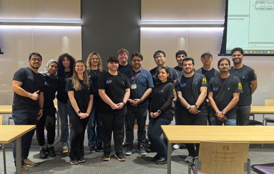 More than a dozen student researchers stand with Assistant Professor Abdullah Canbaz inside the ETEC shared training room.