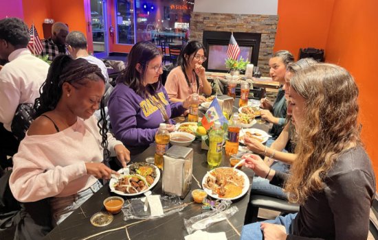 Students are seated at a table in a restaurant eating plates of Haitian food.