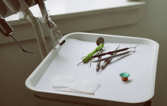 White plastic tray of dental implements including white gauze pads, various metal picks, and a small container of fluoride with a green metallic cap