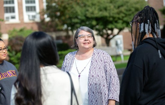 Victoria Rizzo smiles and speaks with three students outside on UAlbany’s Downtown Campus.