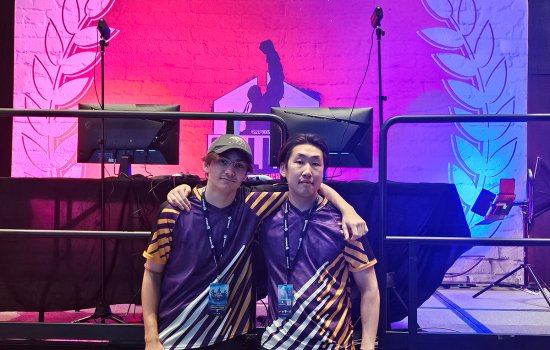Josh Pressano and Kenta Lange stand in front of the game stage in their UAlbany Esports jerseys at the Collegiate Esports Commissioner’s Cup. 