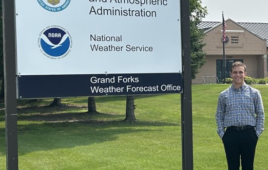 Daniel Harkin stands next to a Grand Forks Weather Forecast Office sign.