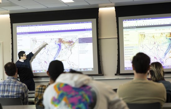 A UAlbany atmospheric science student points to a weather map of the United States.