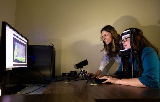 A woman in an apparatus looks at a monitor measuring where her line of sight goes as anothe woman looks on.