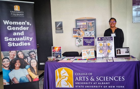 Dr. Janell Hobson is standing behind a table with a University at Albany Women's, Gener and Sexuality Studies banner, showcasing the University's Fall Preview event.