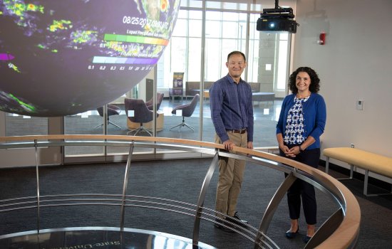 Professors Brian Tang and Kristen Corbosiero stand next to a globe display in the "Science On a Sphere" room at ETEC. 