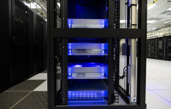 A photo of a black server cabinet with four silver racks illuminated blue from within.
