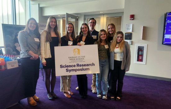 Students from Saratoga Springs High School hold up a Science Research Symposium sign inside UAlbany's Campus Center.
