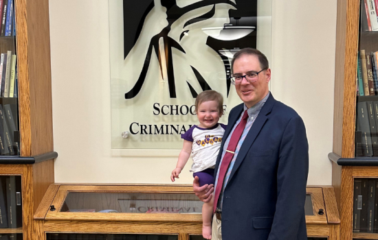 John McCluskey stands with his granddaughter in front of a sign for the School of Criminal Justice. 