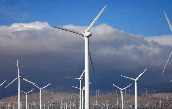 A field of wind turbines with dark clouds above them.