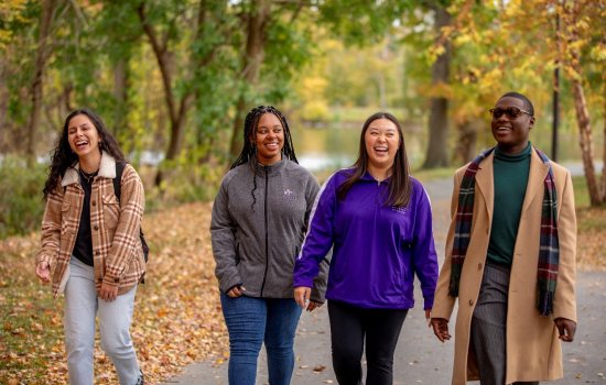 Four UAlbany students laughing while walking a fall colorful, foliaged path.