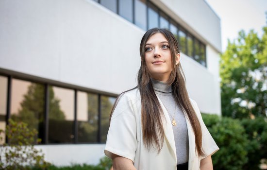 Student Cassie Kane stands in front of the School of Public Health, looking to the side.