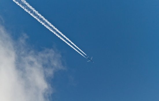 Thin white clouds form behind a jet across the sky.