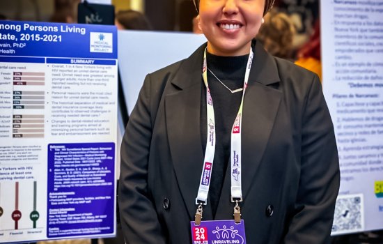Amaal Alharbi smiles and poses for a photo in fromt of her research poster at a professional conference.
