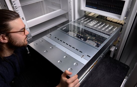 A person in the foreground slides a metallic silver computer node into a server rack.