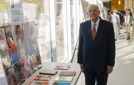 A man in a suit and tie and wearing glasses stands next to a table topped with books below a sign that reads "The Department of Africana Studies Faculty Publications"