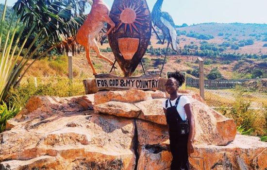 Zari Ward stands in Uganda next to the Ugandan coat of arms.