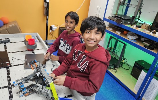 Two boys smile as they assemble a robot on a game board.