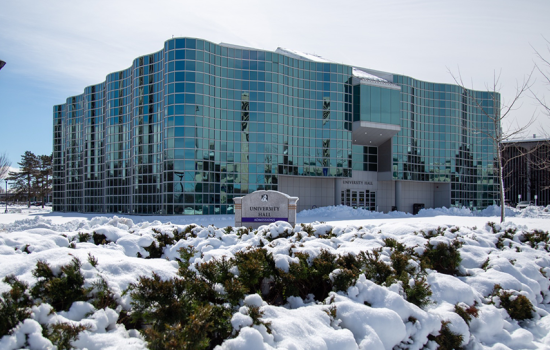 University Hall on a snowy day. The large building's glass windows gleam in the sunlight, reflecting the snowy landscape.
