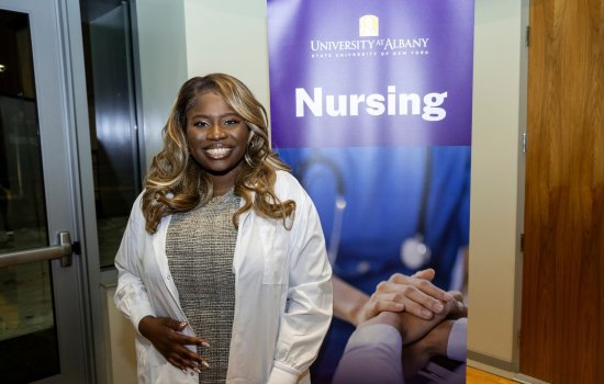 A nursing student stands in front of a poster that says "Nursing".