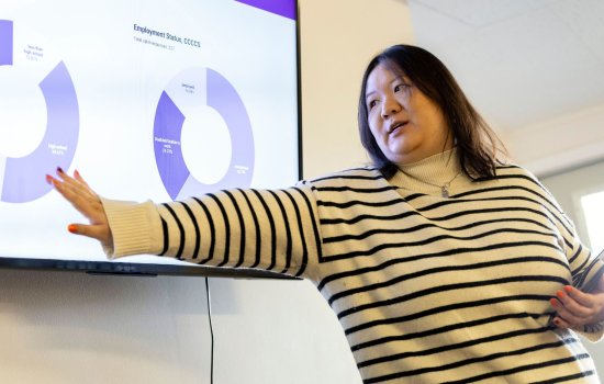 Zhi Chen points to a screen, where a statistic related to her work is shown in a visual representation made out of purple segments that make up a circle.