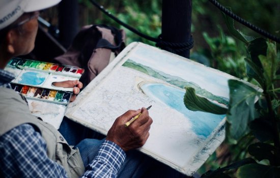 A person uses watercolors to paint a beach scene.