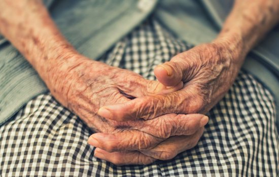 An older adults sits with her hands in her lap.