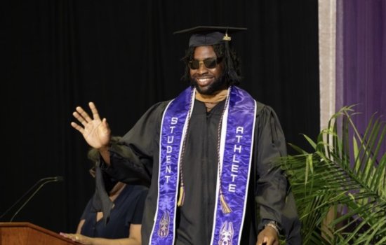 Student is wearing cap and gown, waving at the audience