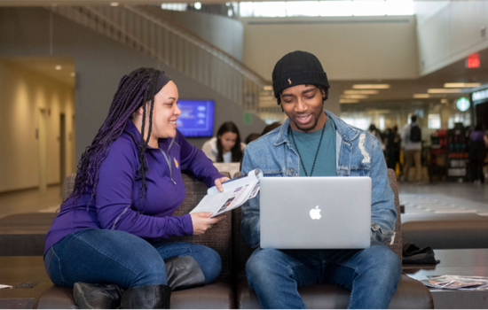 Twi student sit in Campus Center, talking to each other about what they're looking at on a laptop and some paper.