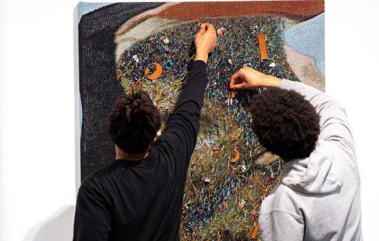 Two young African American students work with a fabric art piece in the University Art Museum by artist Noel W Anderson.