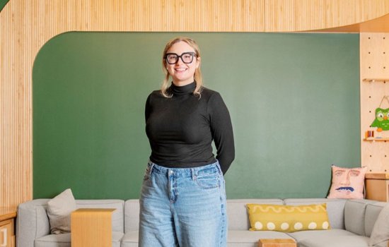 Adele standing in front of a couch with a green board behind it.