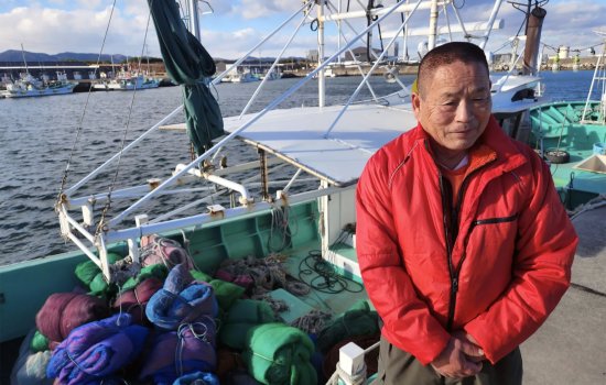 Haruo Ono a weathered man from Japan stands in front of his fishing trawler at Shinchi harbor, Fukushima.