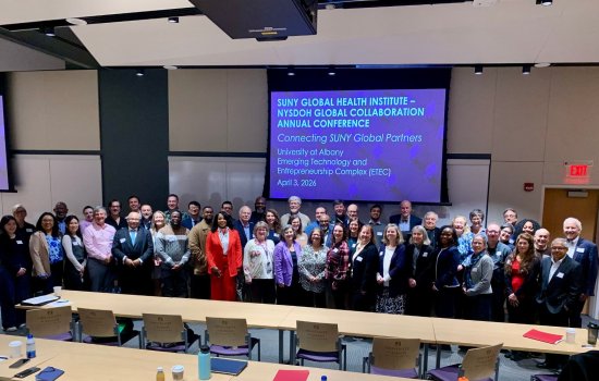 Conference members stand together in a conference room, in front of a presentation screen.