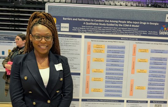 A portrait of Busayo at UAlbany Showcase. She stands in front of her academic poster, which displays information about her work in Georgia.