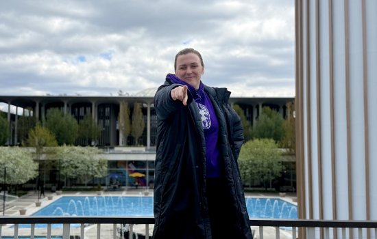 Zoe Veaunt stands above the main fountain wearing a Damien sweatshirt and pointing at the camera.