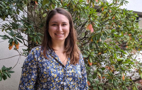 Taylor Perre, wearing a blue and yellow floral shirt, poses for a portrait photograph in front of shrubbery.