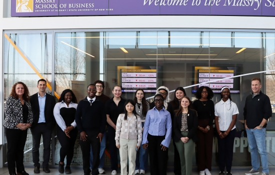 A group of people stand inside the Massry School of Business at the Unviersity at Albany posed for a group shot.